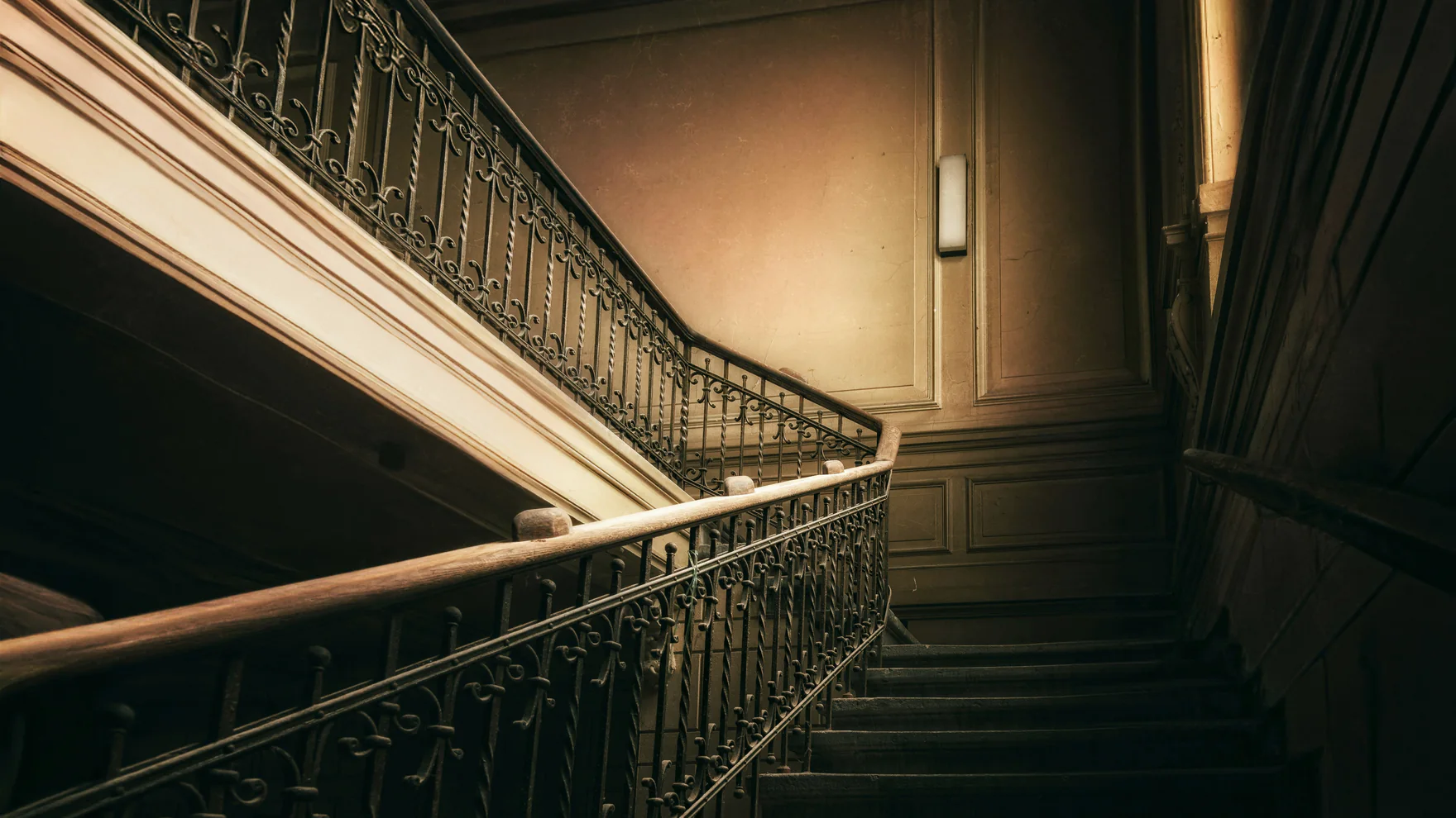 Cage d’escalier d’un immeuble ancien : rampe en fer forgé et main courante en bois