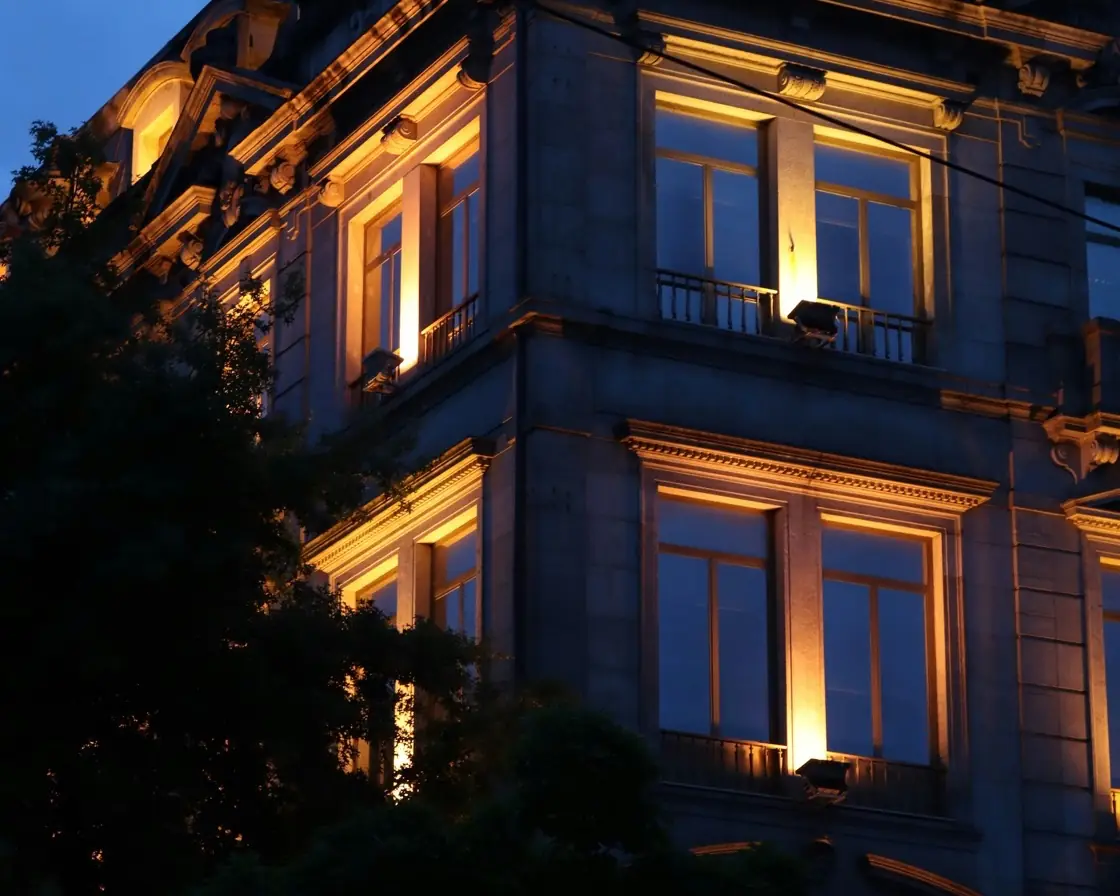 Façade en pierre d’un immeuble ancien, fenêtres éclairées à la tombée du jour