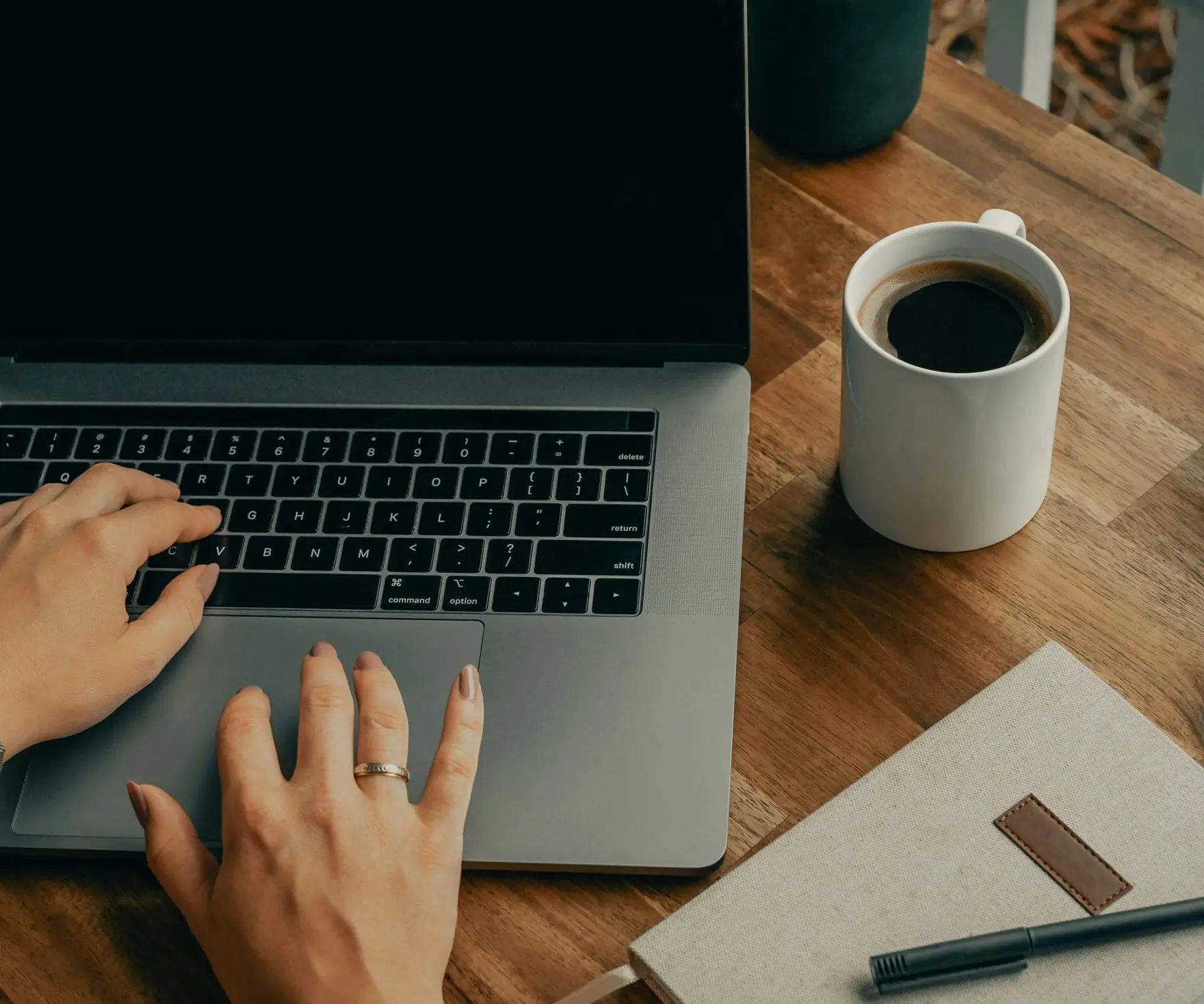 Mains sur le clavier d’un ordinateur portable, tasse de café et carnet sur un bureau en bois